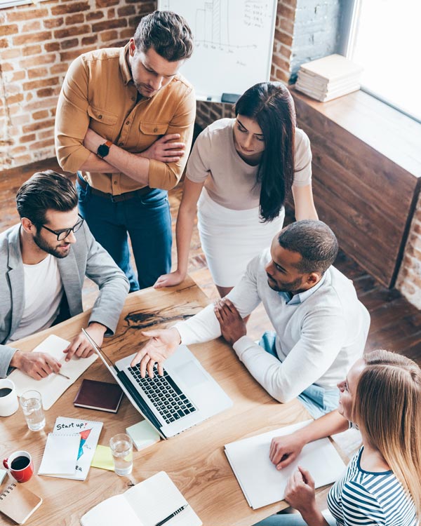 Top view of group of five young people discuss something and gesturing while leaning to the table in office