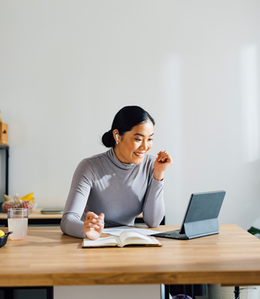 Happy Asian woman using digital tablet for online meeting while sitting in a modern kitchen.