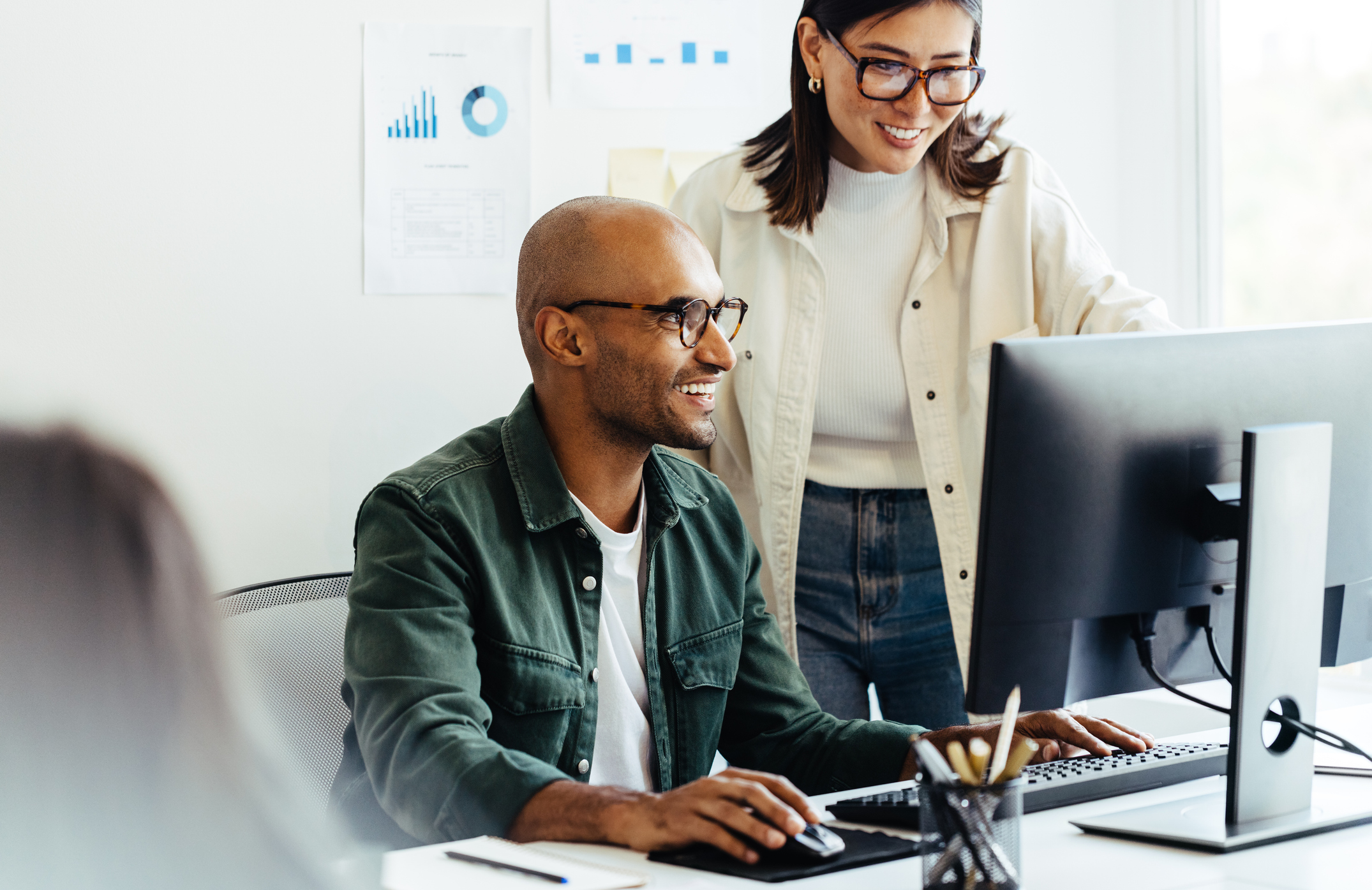 Two digital marketing specialists sitting at a computer discussing the differences between Cost Per Click (CPC) and Cost Per Mille (CPM) advertising strategies.